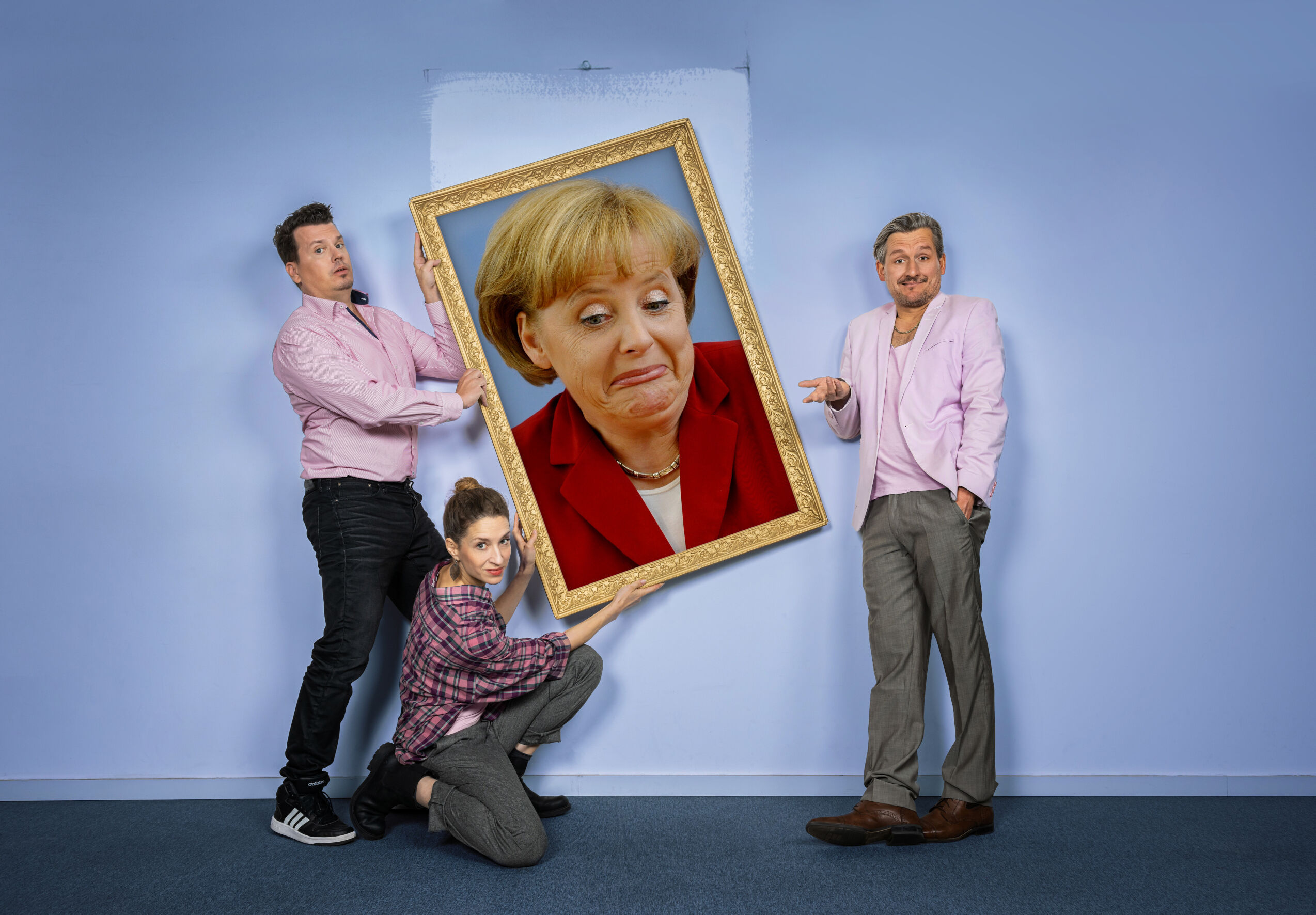 Zwei Personen halten ein Porträt von Ex-Kanzlerin Merkel