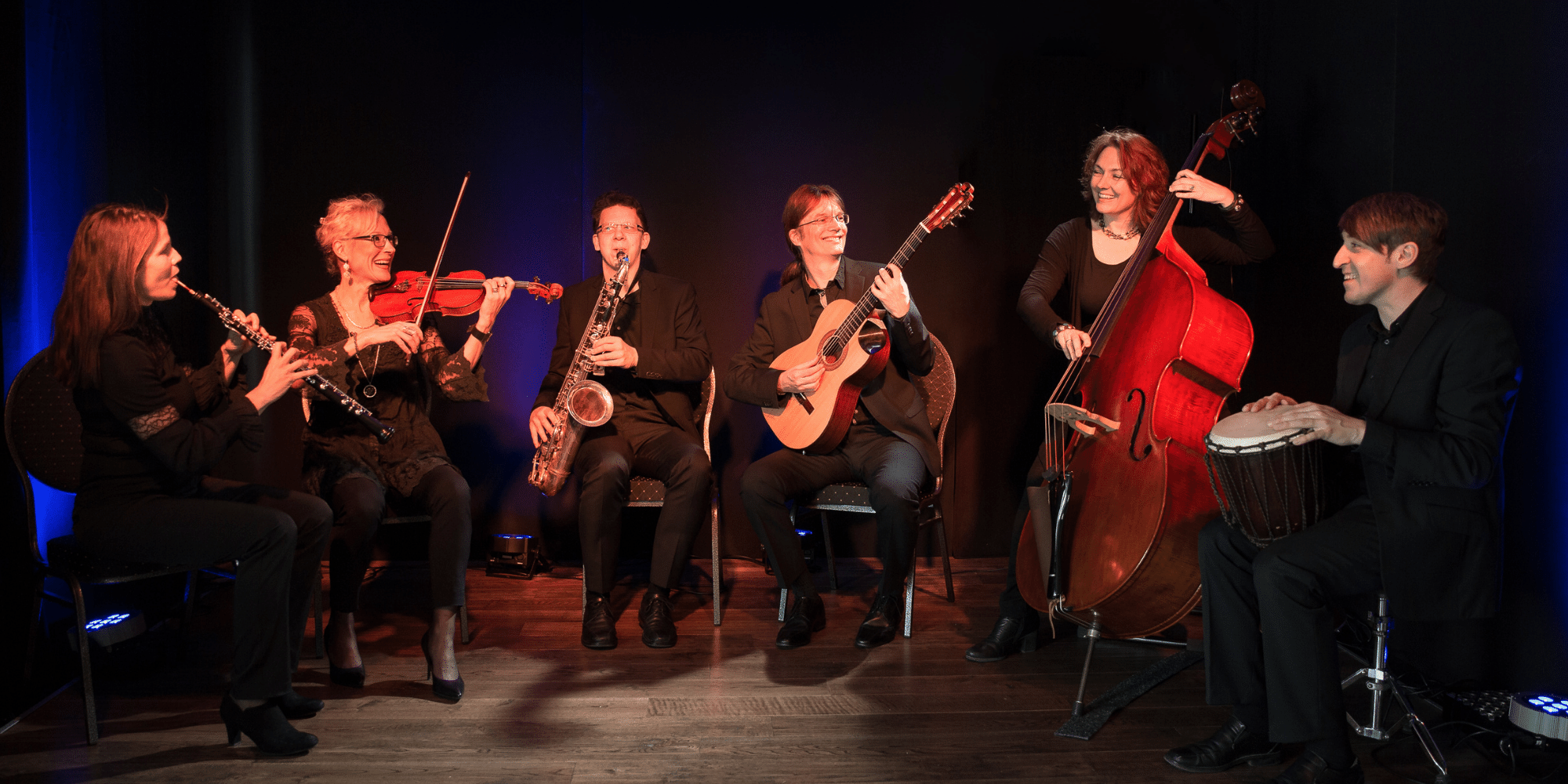 Mehrere Musiker mit Musikinstrumenten auf einer Bühne sitzend