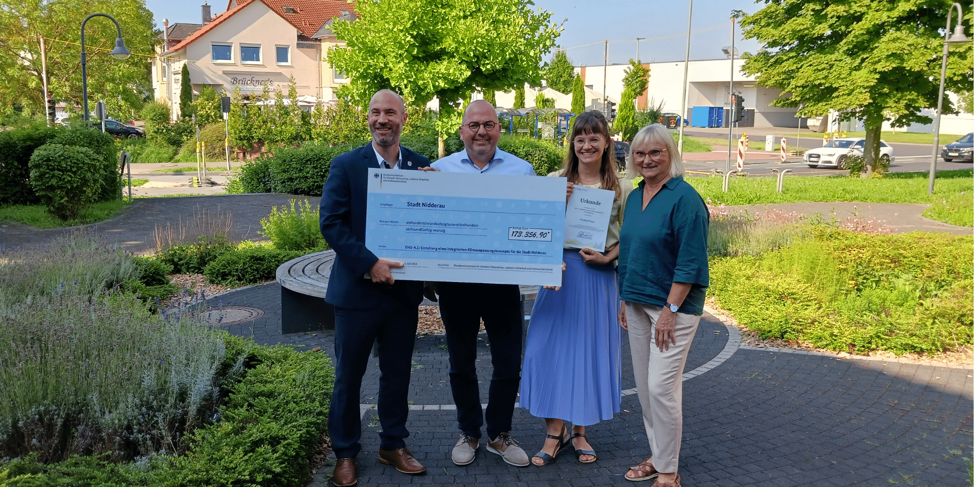 3 Personen stehend vor dem Rathaus mit großem Spendenscheck