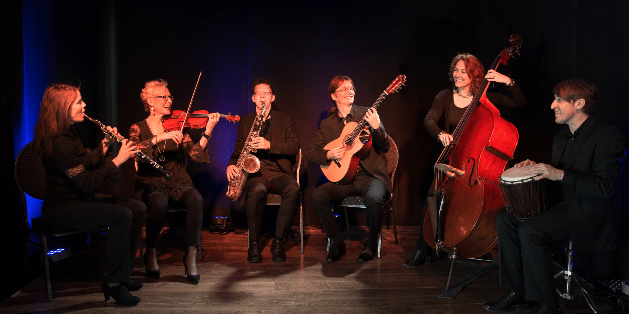Musiker sitzend auf einer schwarzen Bühne mit ihre  Musikinstrumenten