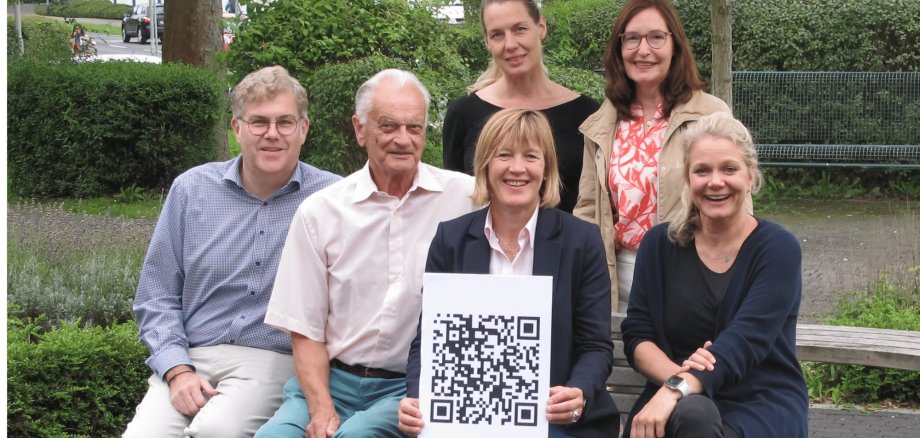 Mehrere Personen sitzend mit einem weiß-schwarzen Poster haltend