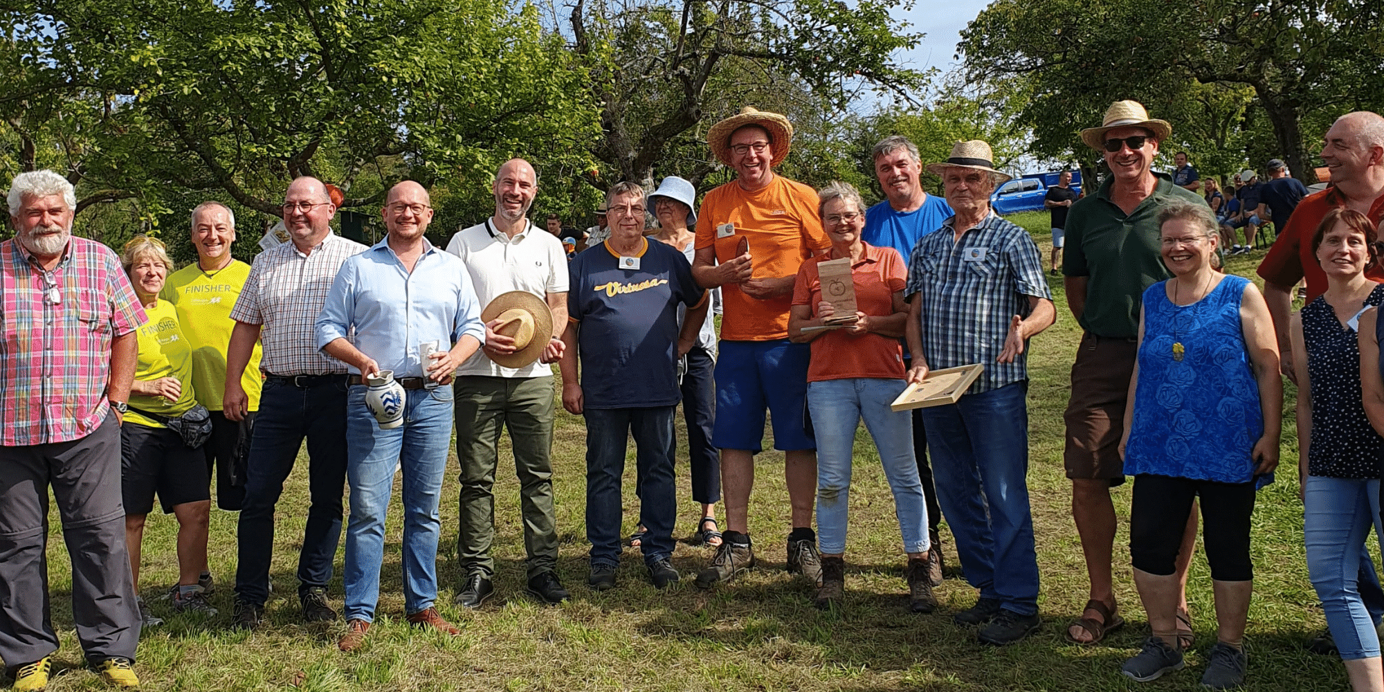 Mehrere Personen stehend auf einer Wiese umgeben von Obstbäumen