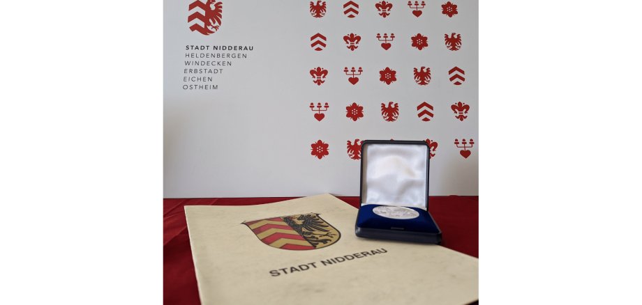 Medaille und Urkunde liegend auf einem Tisch mit rotem Tischtuch