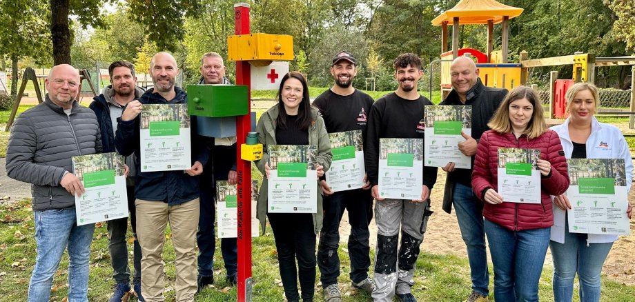 10 Personen stehen auf Spielplatz neben Pfahl für alle Fälle und halten Plakate hoch