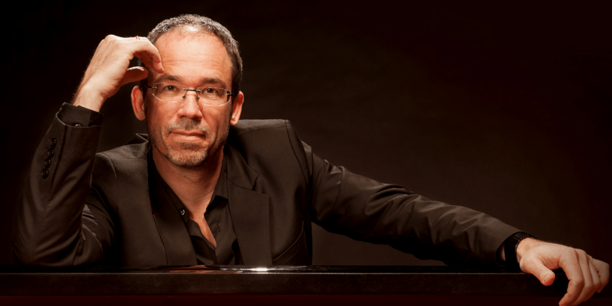 Mann in schwarzem Anzug und Brille sitzend 