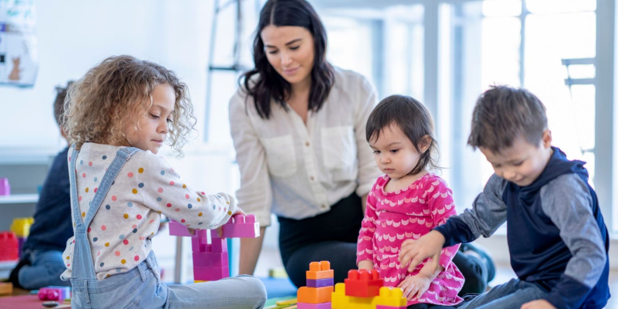 Frau auf dem Boden sitzend mit spielenden Kindern mit Bauklötzen