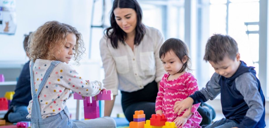 Frau auf dem Boden sitzend mit spielenden Kindern mit Bauklötzen