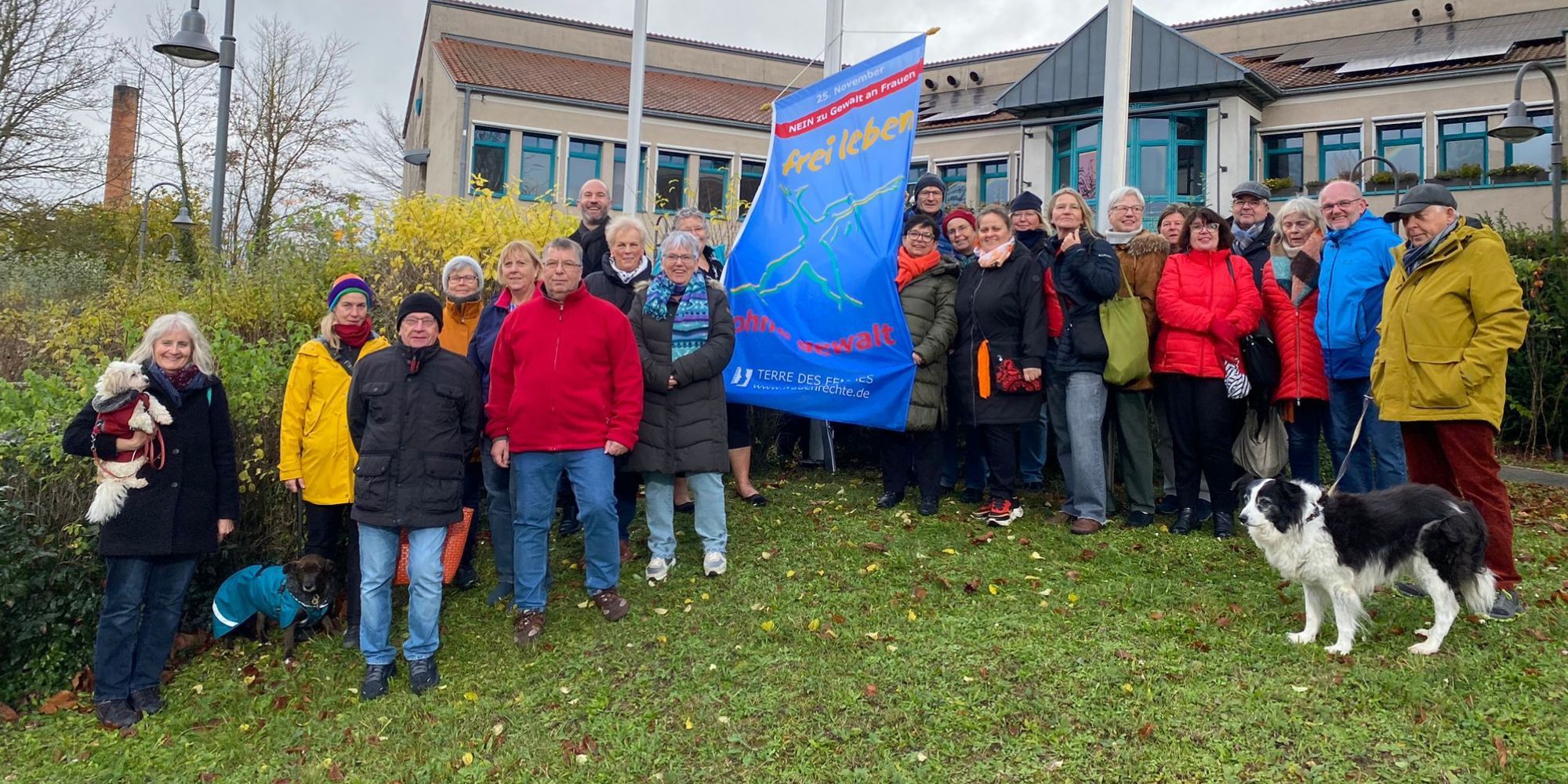 Menschengruppe mit Aktionsfahne Terre des Femmes neben Fahnenmast