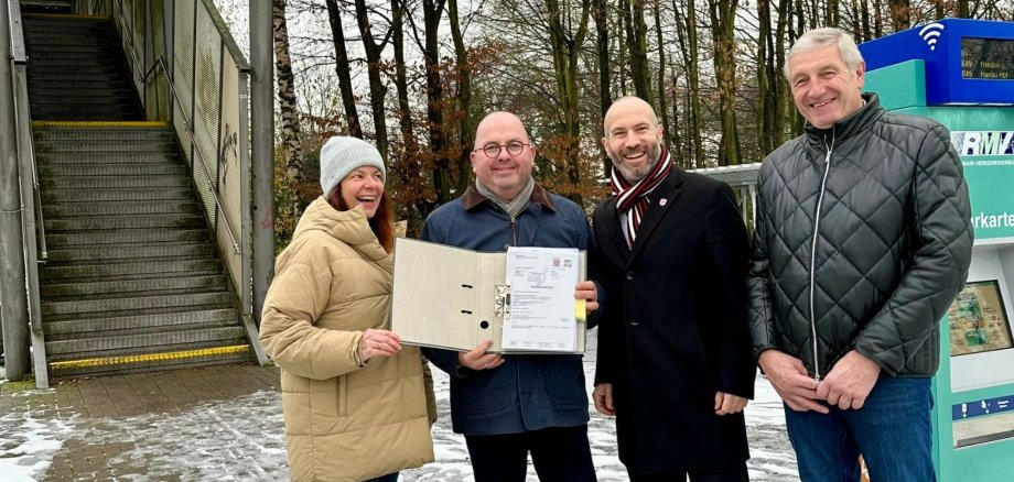 4 Menschen stehen vor einem Fahrkartenautomaten und halten Förderbescheid in die Kamera