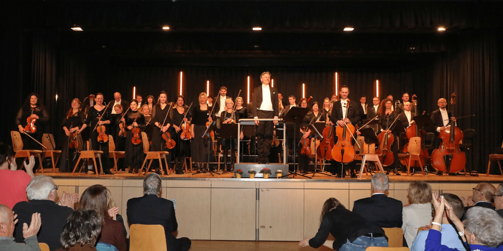 Mehrere in schwarz gekleidete Personen sitzend mit Musikinstrumenten auf einer Bühne