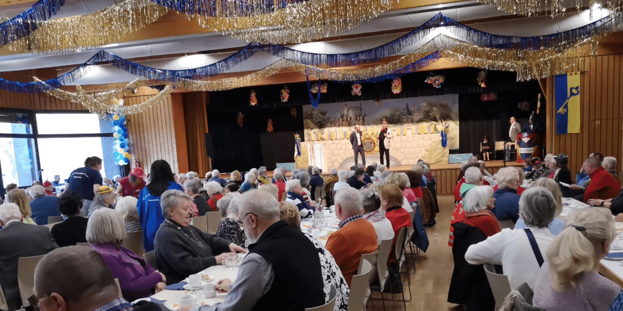 Mehrere ältere Menschen sitzend in einem festlich geschmückten Saal