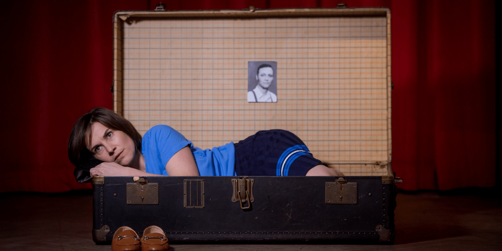 Frau mit blauem T-Shirt liegend in einem Koffer