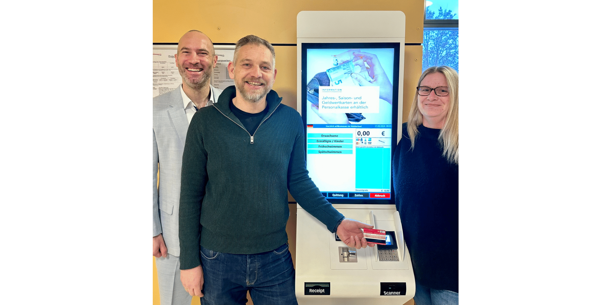 Drei Personen stehend vor einem Bezahlterminal. Ein Mann hält eine rote Karte an das Bezahlterminal