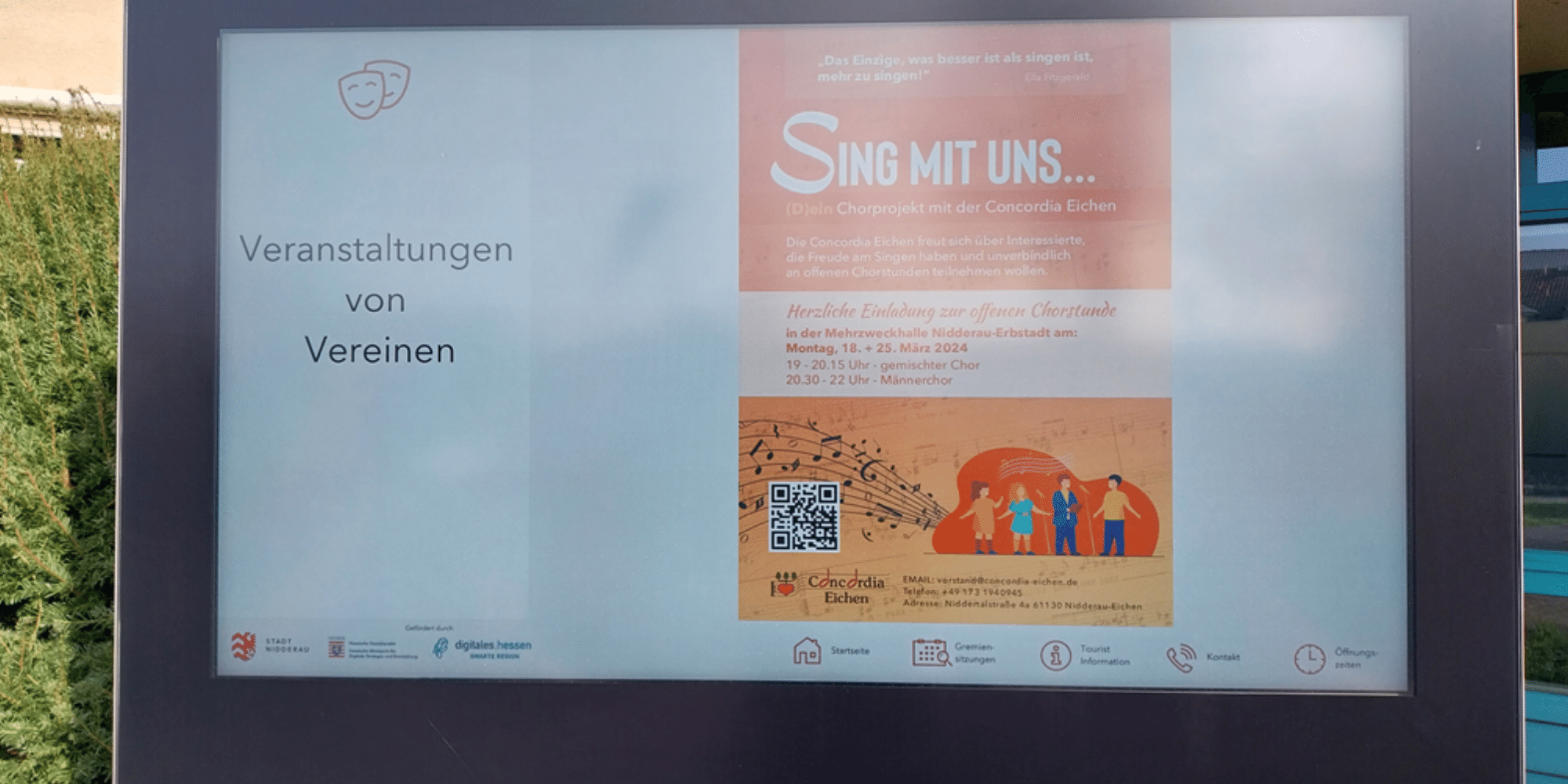 Digitales Display vor dem Rathaus mit einem orangenen Plakat einer Vereins-Veranstaltung