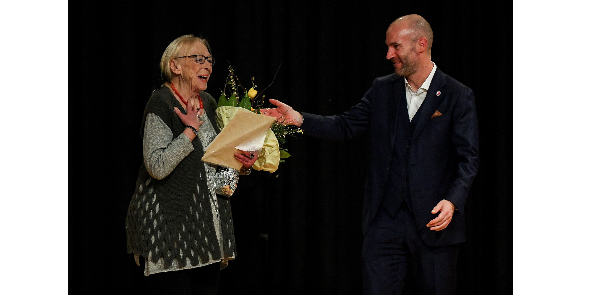 Ein Mann überreicht einer Frau Blumen auf einer Bühne.