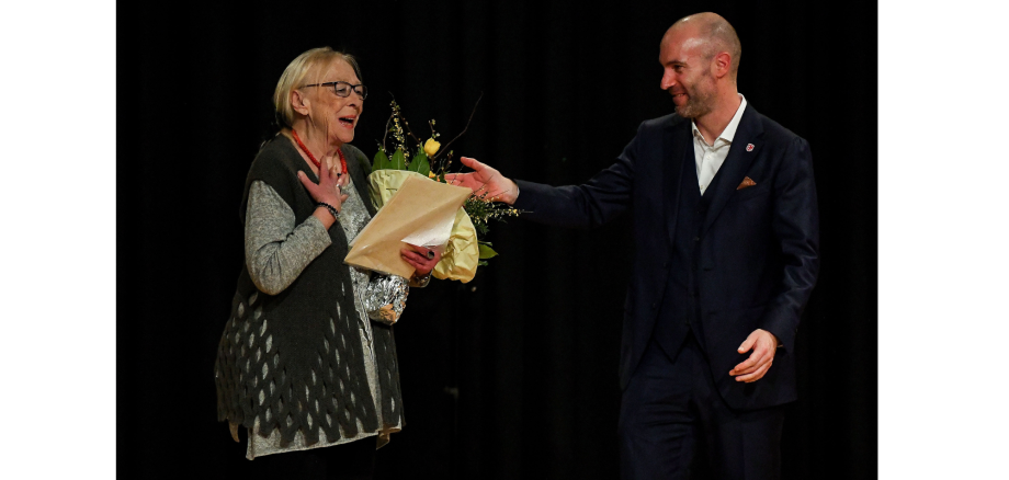 Ein Mann überreicht einer Frau Blumen auf einer Bühne.