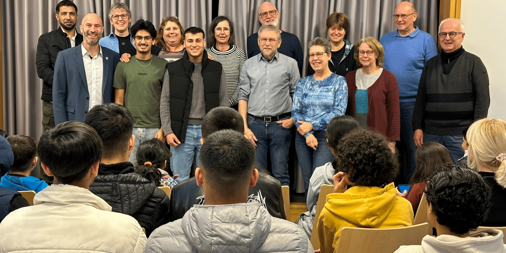 Mehrere Personen stehend vor einigen Personen sitzend in einem Raum