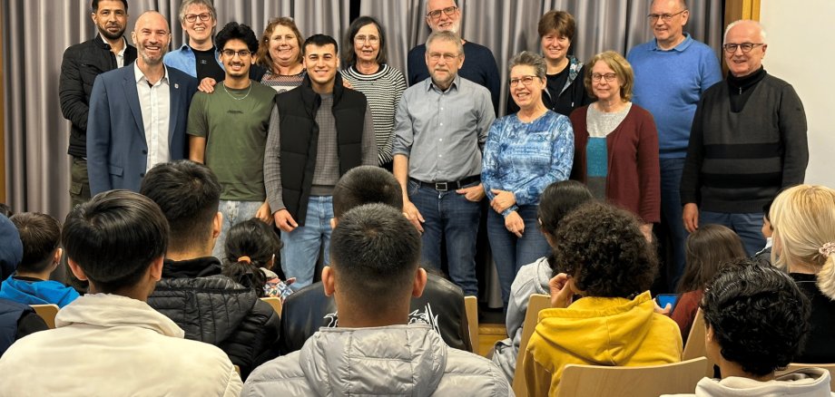 Mehrere Personen stehend vor einigen Personen sitzend in einem Raum