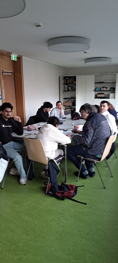 Mehrere Personen sitzend an einem Tisch mit ausgebreiteten Arbeitsmaterialien darauf