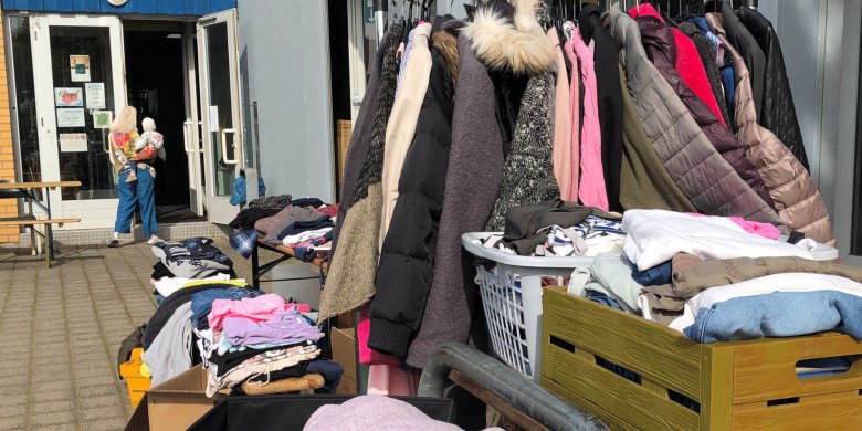 Kleidungsstücke an einem Kleiderständer und in Kartons vor einer Hausfassade dargeboten