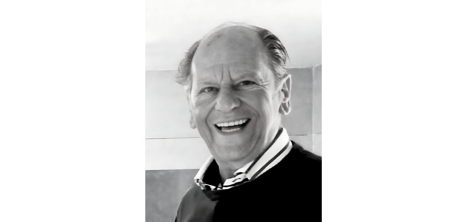 Porträt eines Mannes lächelnd mit dunklem Pullover, das Foto ist eine schwarz-weiß-Aufnahme