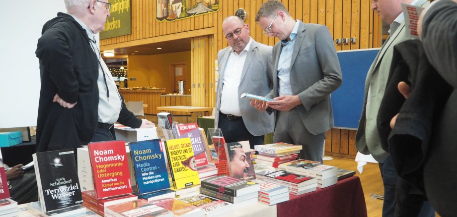 Mehrere Männer stehend vor einem Tisch mit vielen Büchern