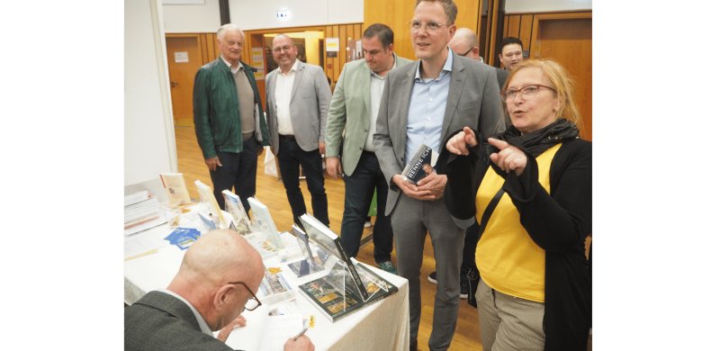 Mehrere Personen stehend vor einem Tisch mit einigen Büchern
