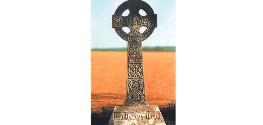 Altes Kreuz aus Stein vor einem Feld