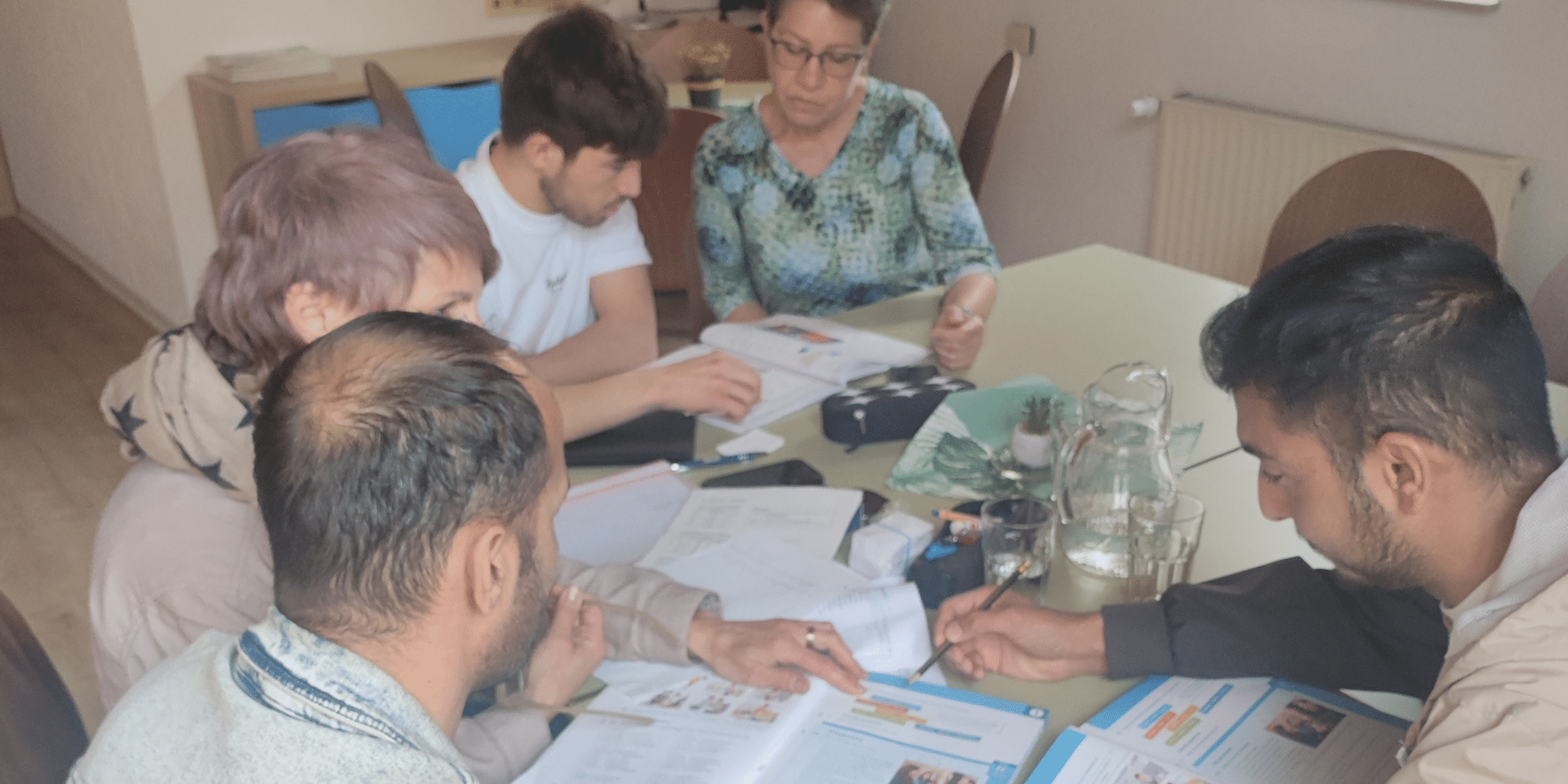 Drei Männer und zwei Frauen sitzend an einem Tisch mit Schulbüchern vor sich liegend