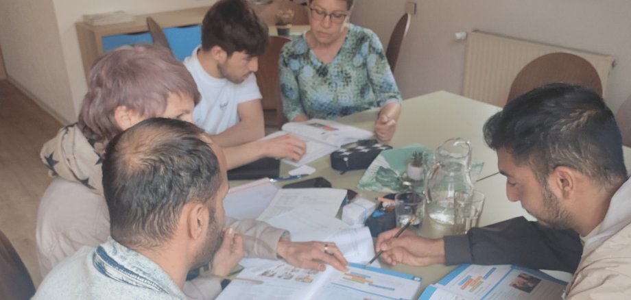 Drei Männer und zwei Frauen sitzend an einem Tisch mit Schulbüchern vor sich liegend