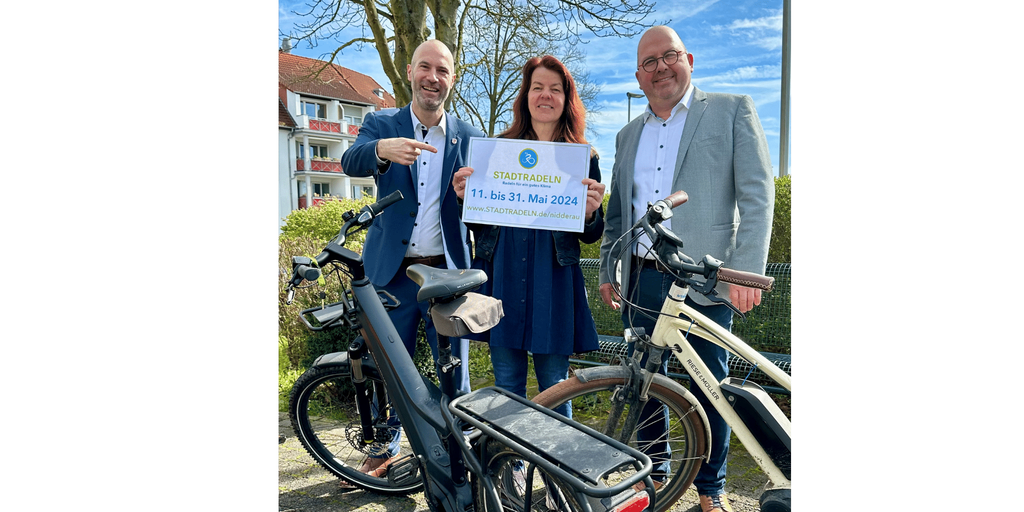 Zwei Männer und eine Frau stehend hinter zwei Fahrrädern. Die Frau hält ein Schild hoch mit der Aufschrift "Stadtradeln"