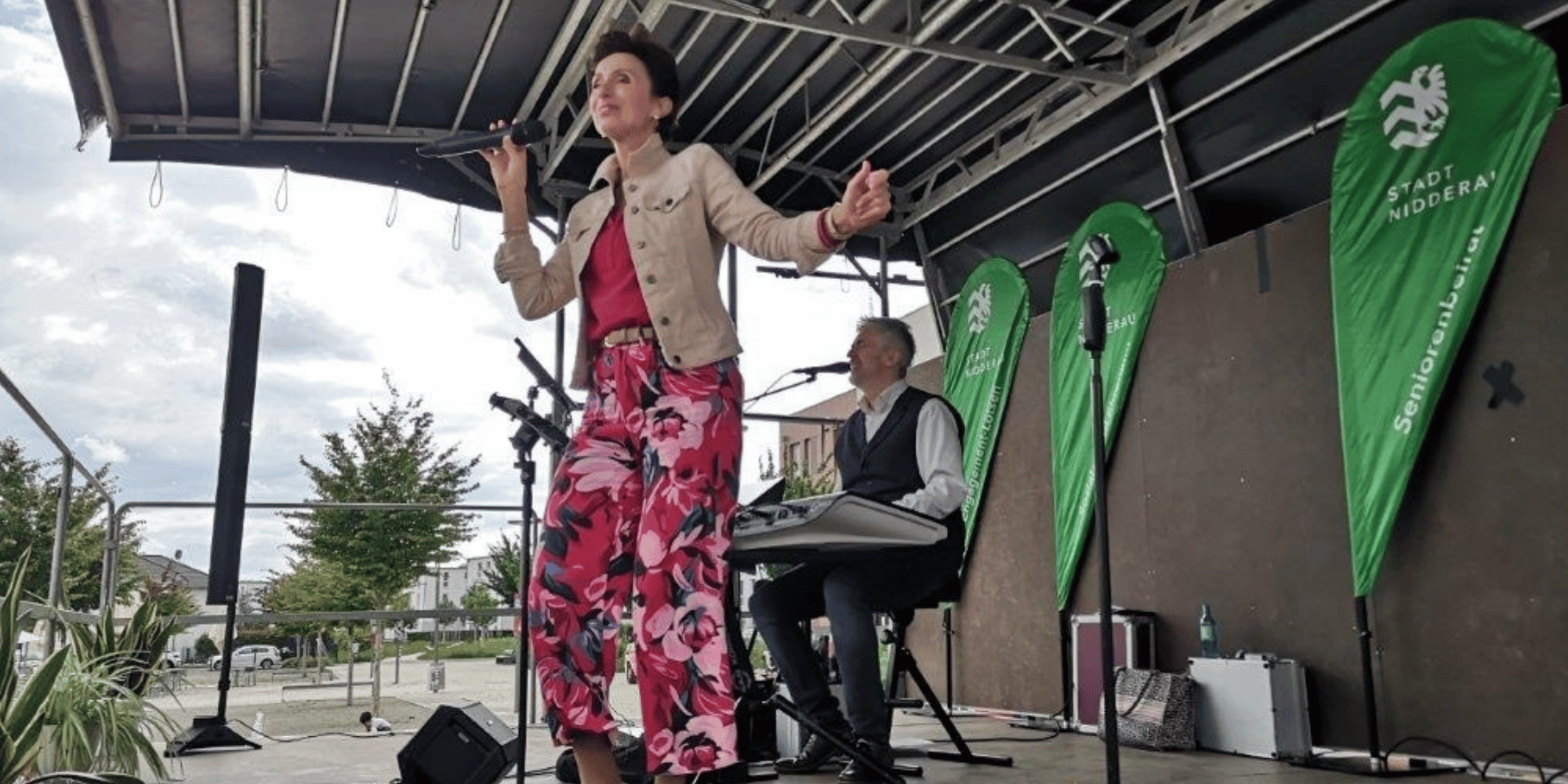 Frau singend und bunt gekleidet mit Mikrofon auf einer mobilen Bühne im Freien