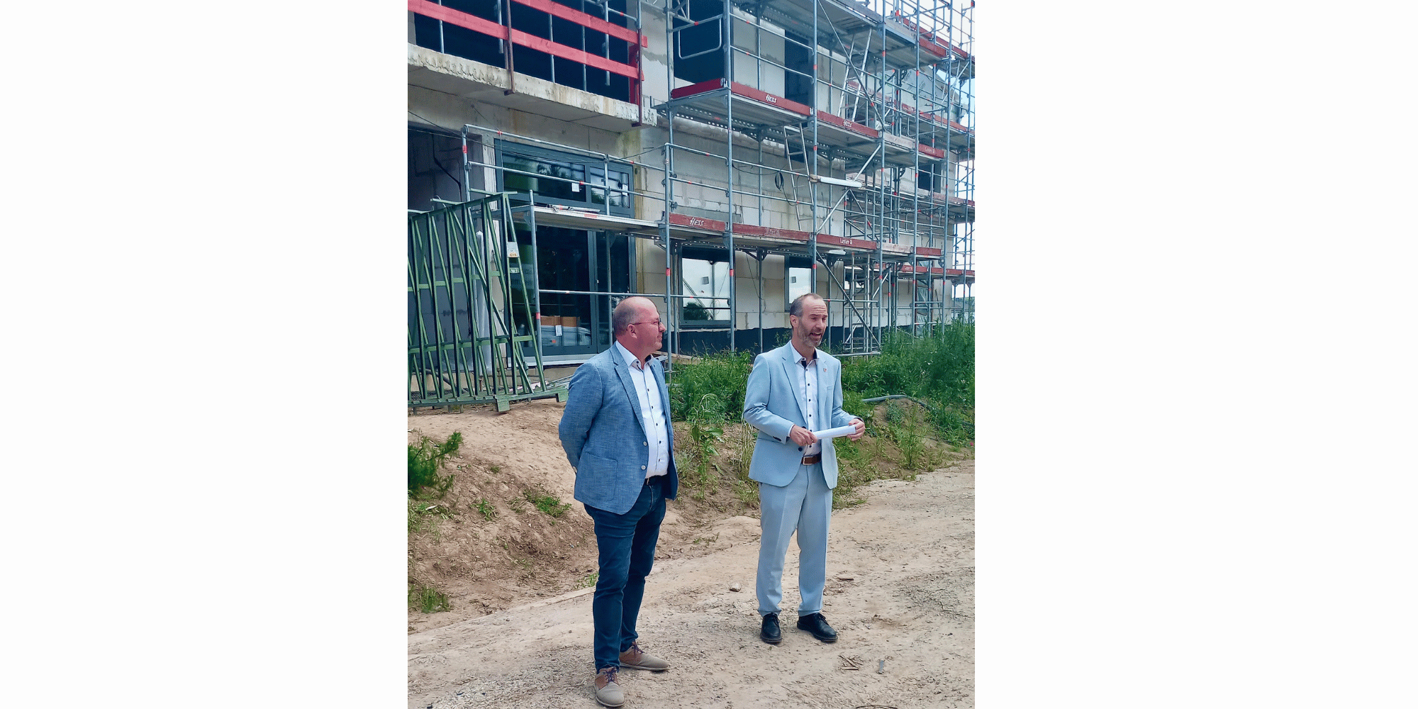 Zwei Männer in Anzügen stehend vor einem Rohbau