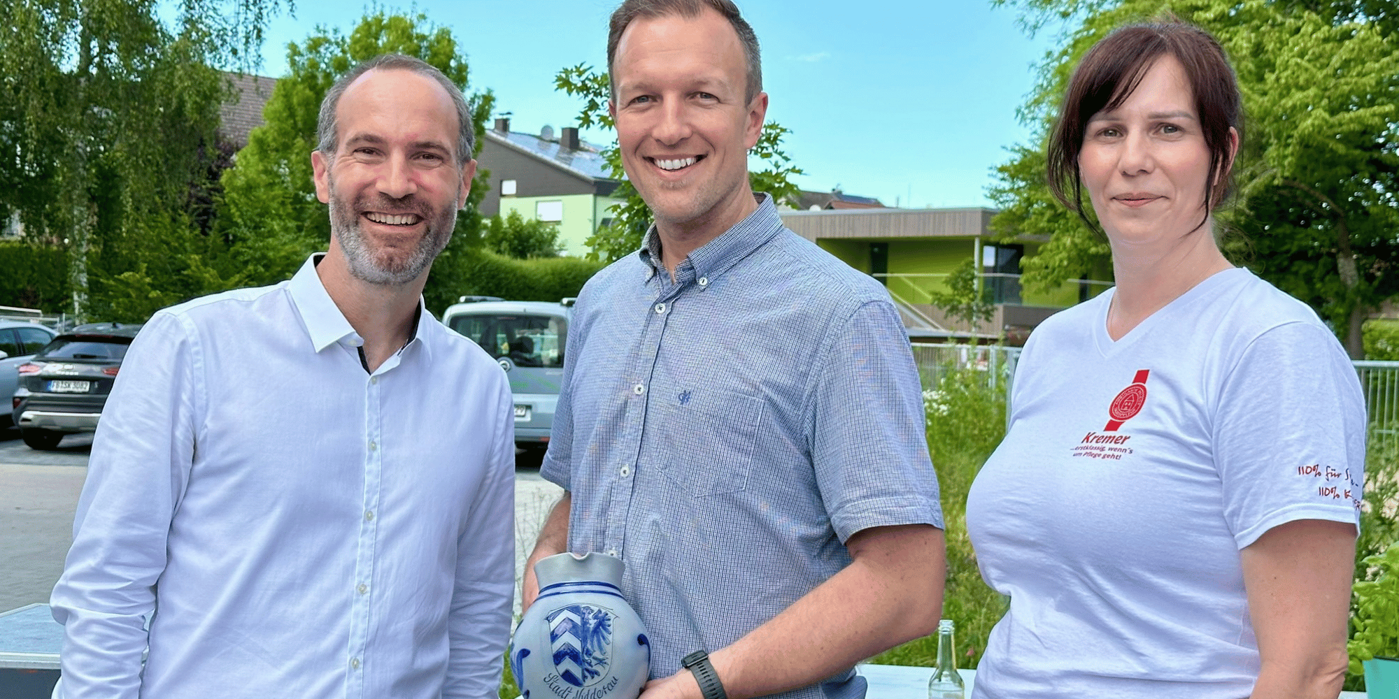 Zwei Männer und 1 Frau stehend. Der Mann in der Mitte hält einen Apfelweinkrug