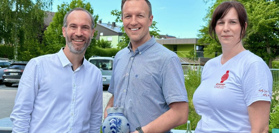 Zwei Männer und 1 Frau stehend. Der Mann in der Mitte hält einen Apfelweinkrug