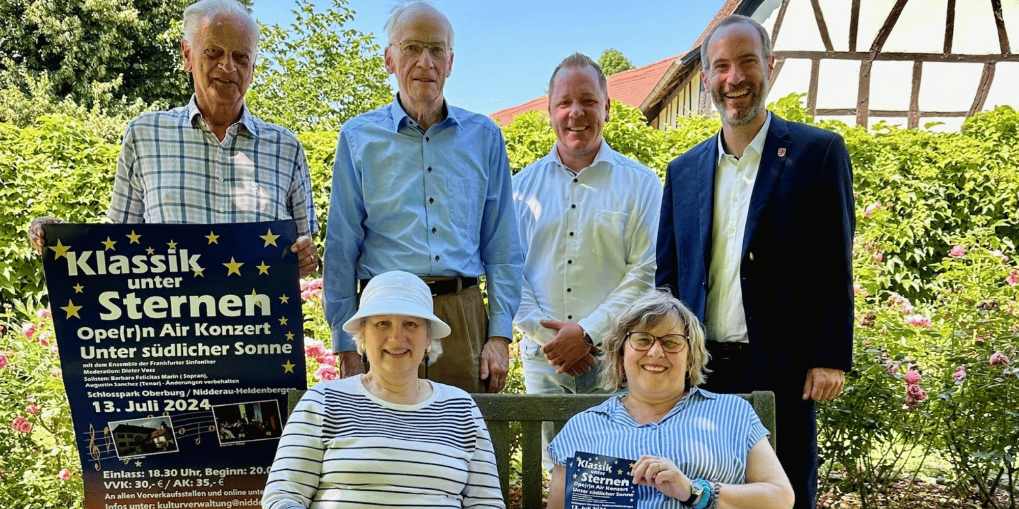 4 Personen stehend und davor 2 Personen sitzend in einem Park