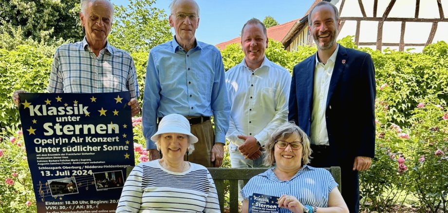 4 Personen stehend und davor 2 Personen sitzend in einem Park