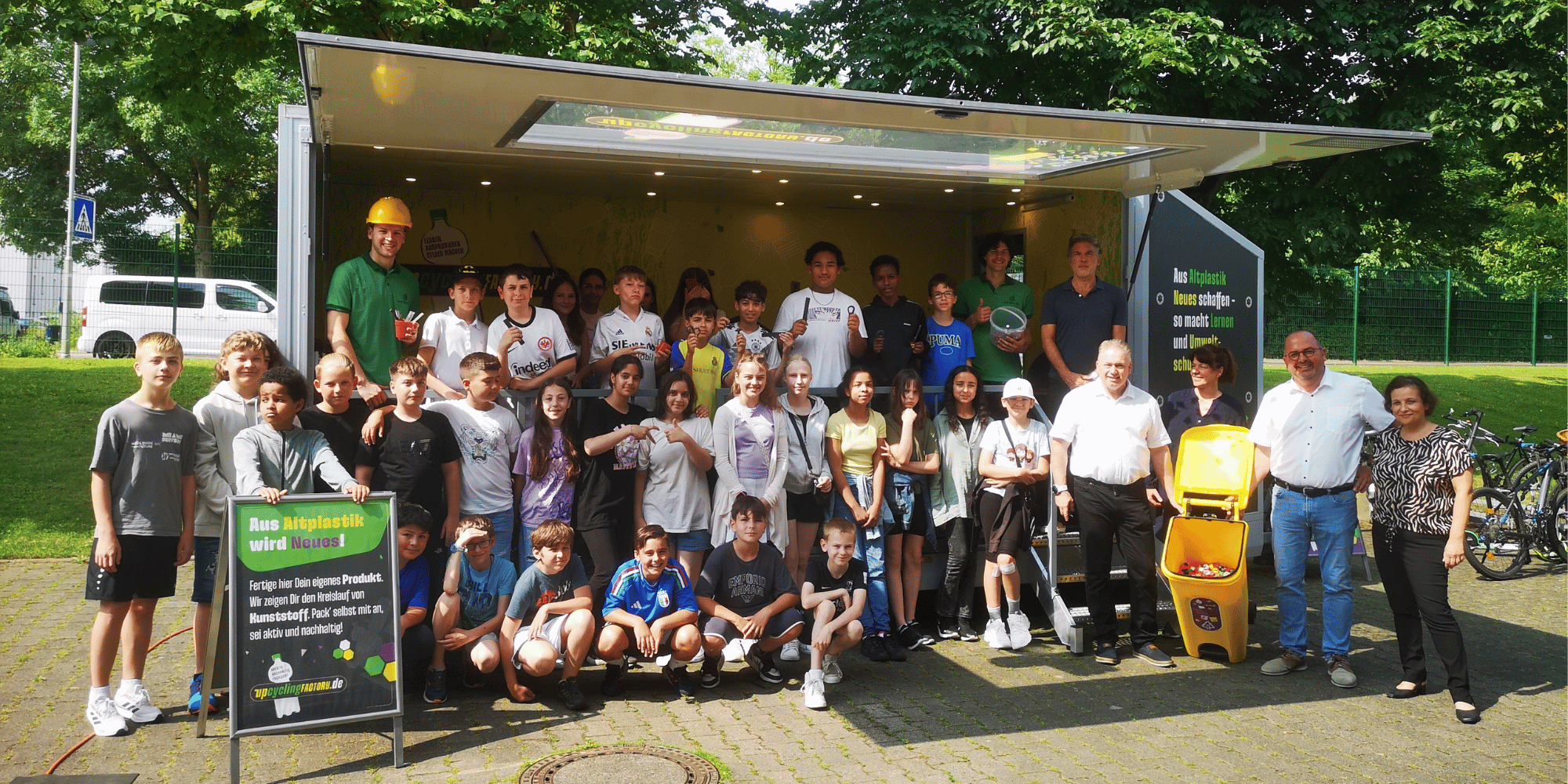 viele Kinder und Erwachsene vor einem Anhänger auf einem Schulgelände