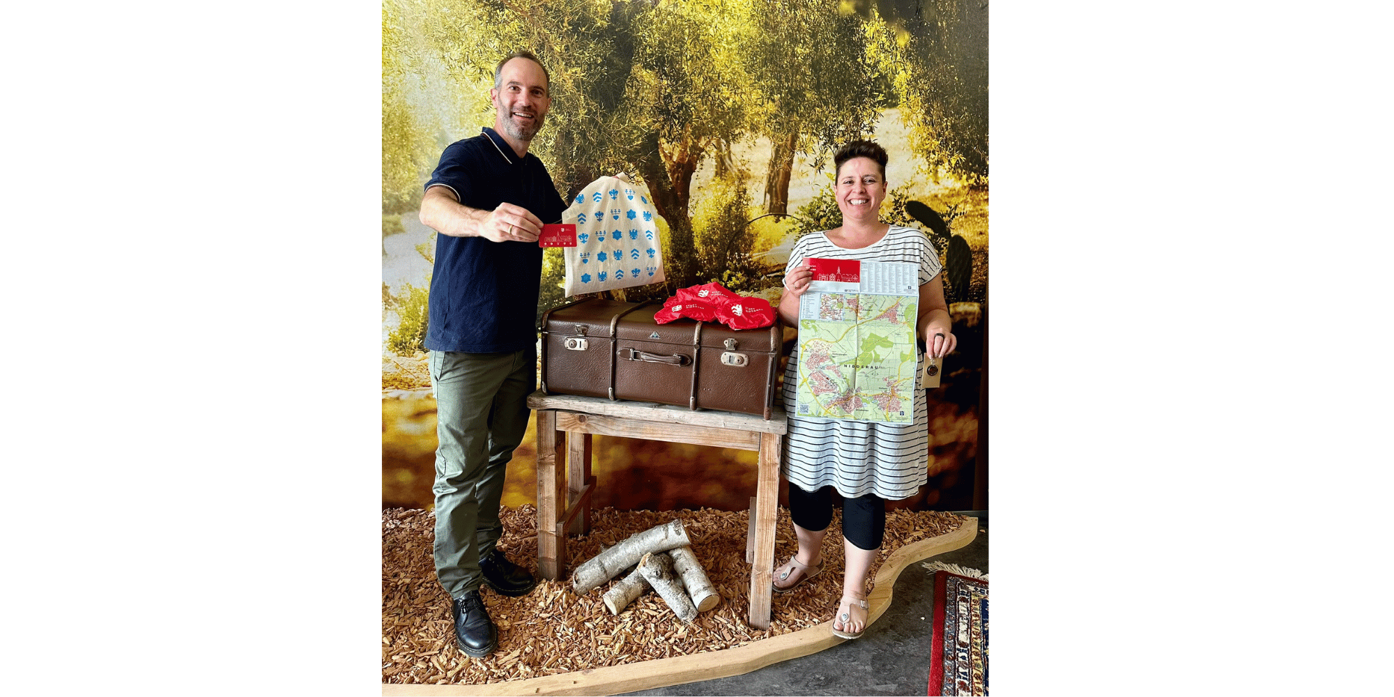 1 Mann und 1 Frau stehend vor einer Fotoleinwand mit Tasche und Stadtplan