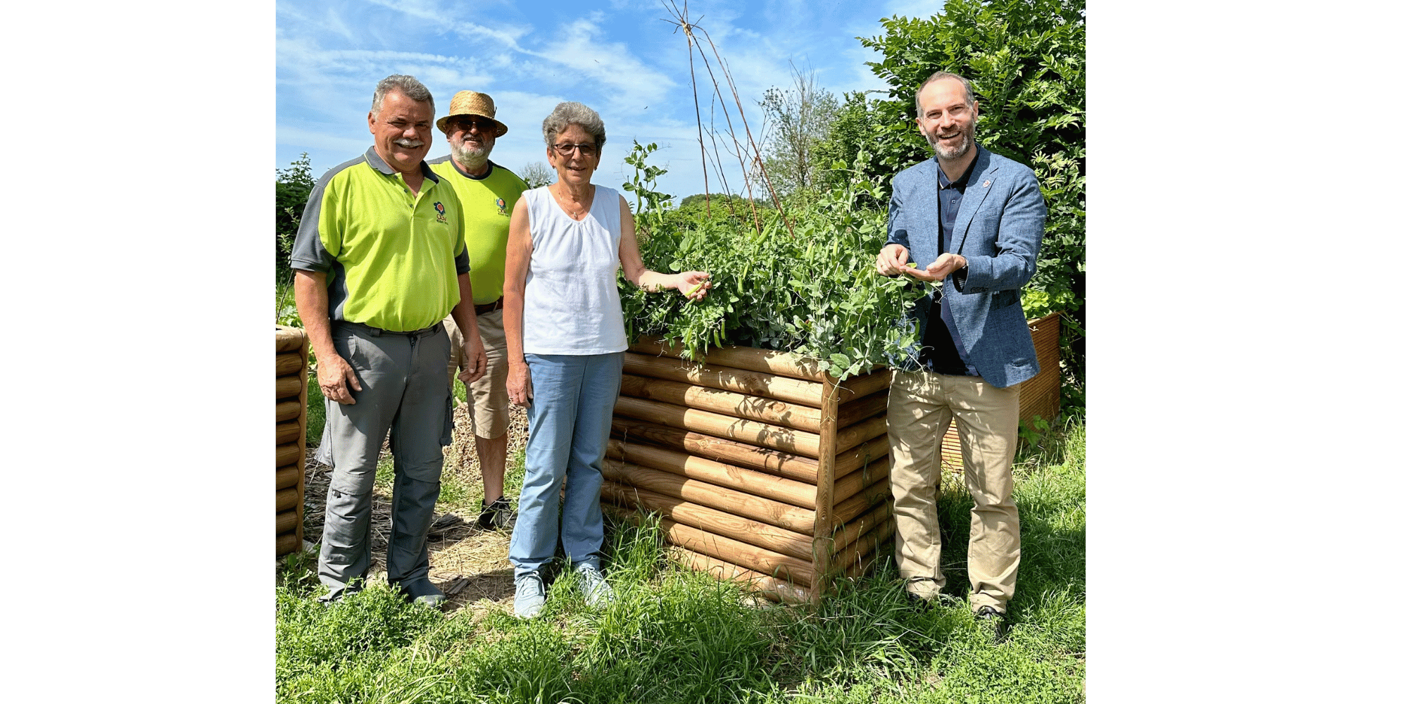 3 Männer und 1 Frau stehend vor einem Hochbeet im Grünen