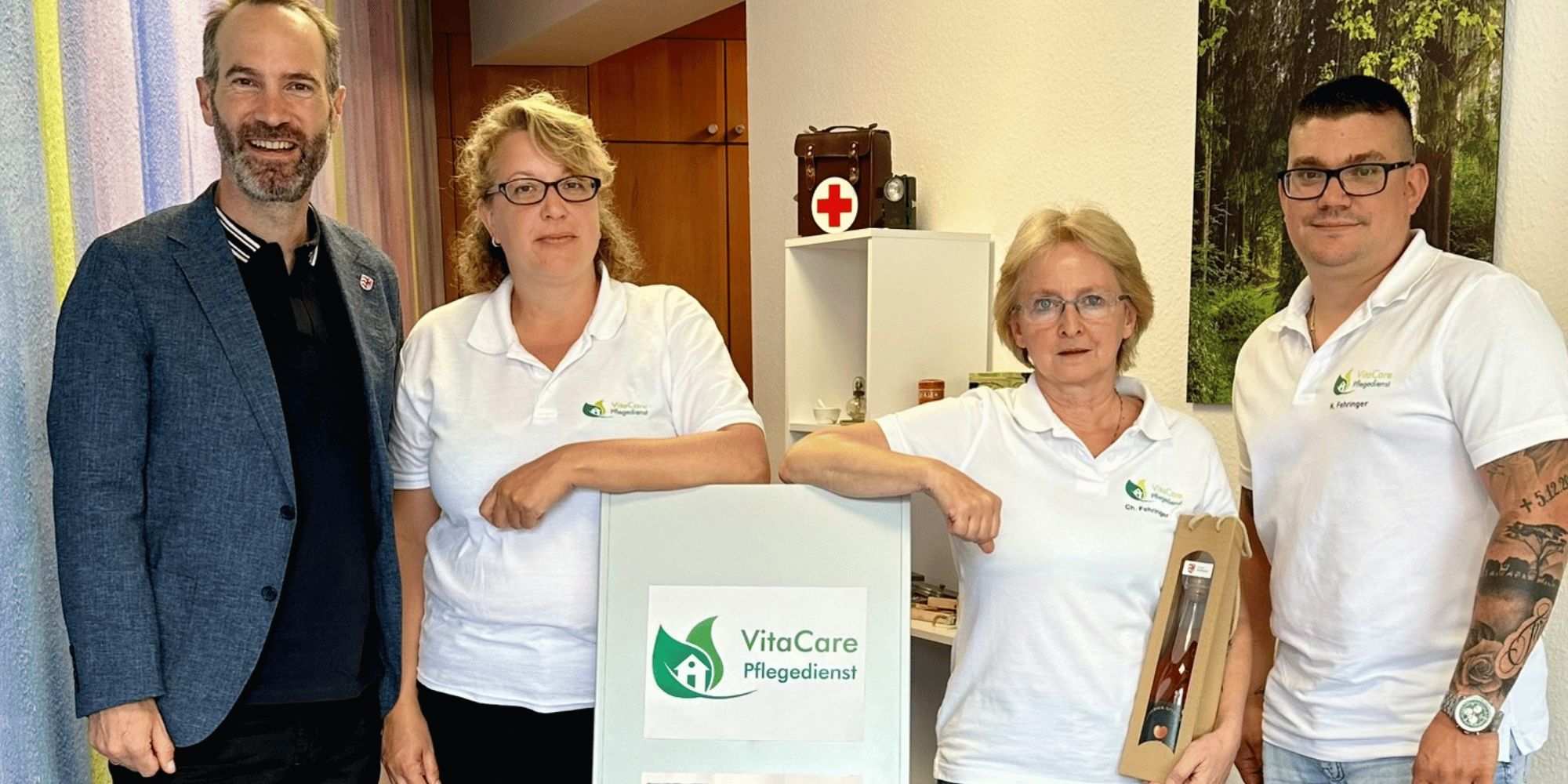 Zwei Männer und zwei Frauen stehend vor einem Plakat mit der Aufschrift Vita Care Pflegedienst