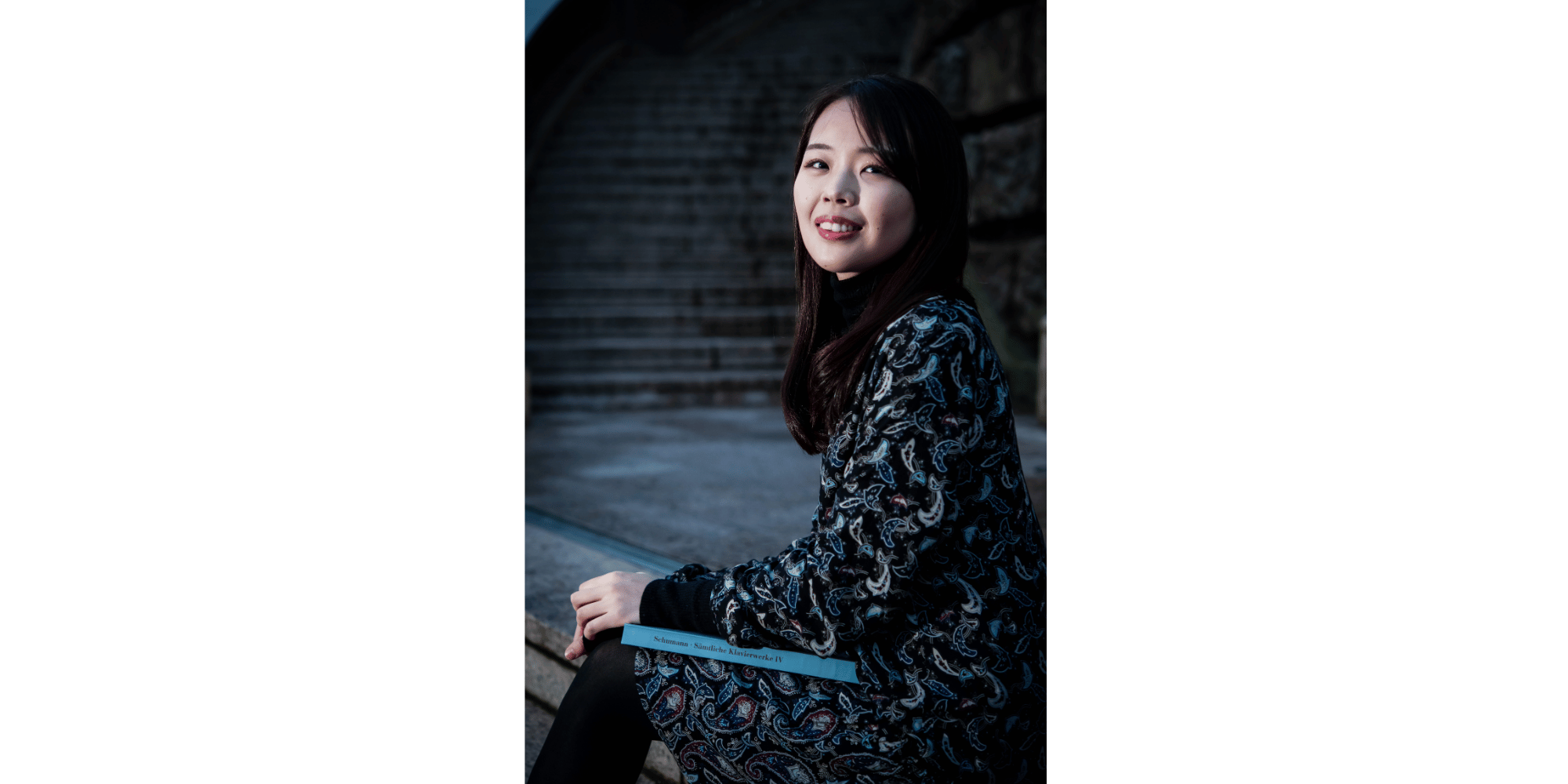 Frau in schwarz gekleidet mit langen schwarzen Haaren, sitzend vor einem Klavier