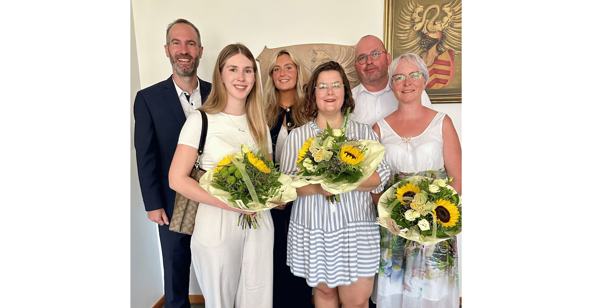4 Frauen und 2 Männer stehend mit Blumen in der Hand