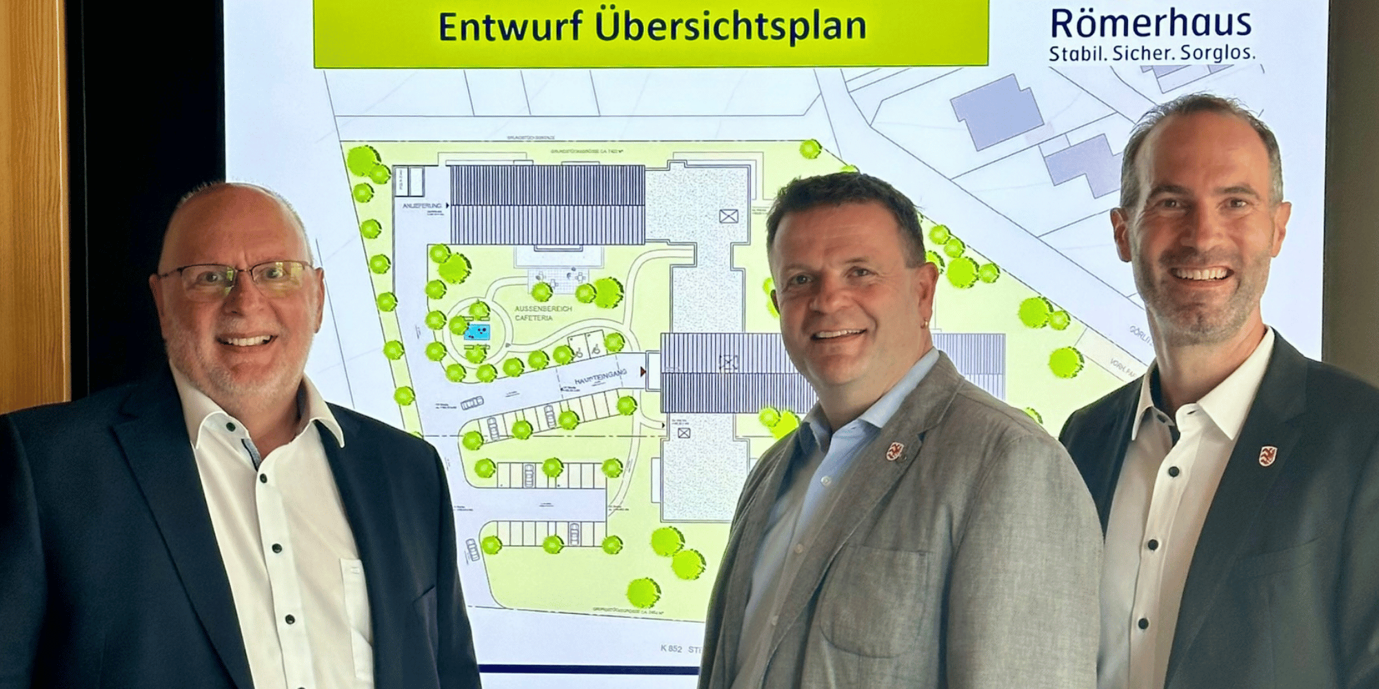 Drei Männer stehend vor einem TV mit einem Entwurfsplan darauf