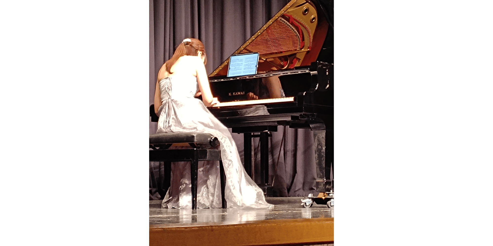 Dame mit schwarzen langen Haaren sitzend in einem hellen Kleid am Klavier