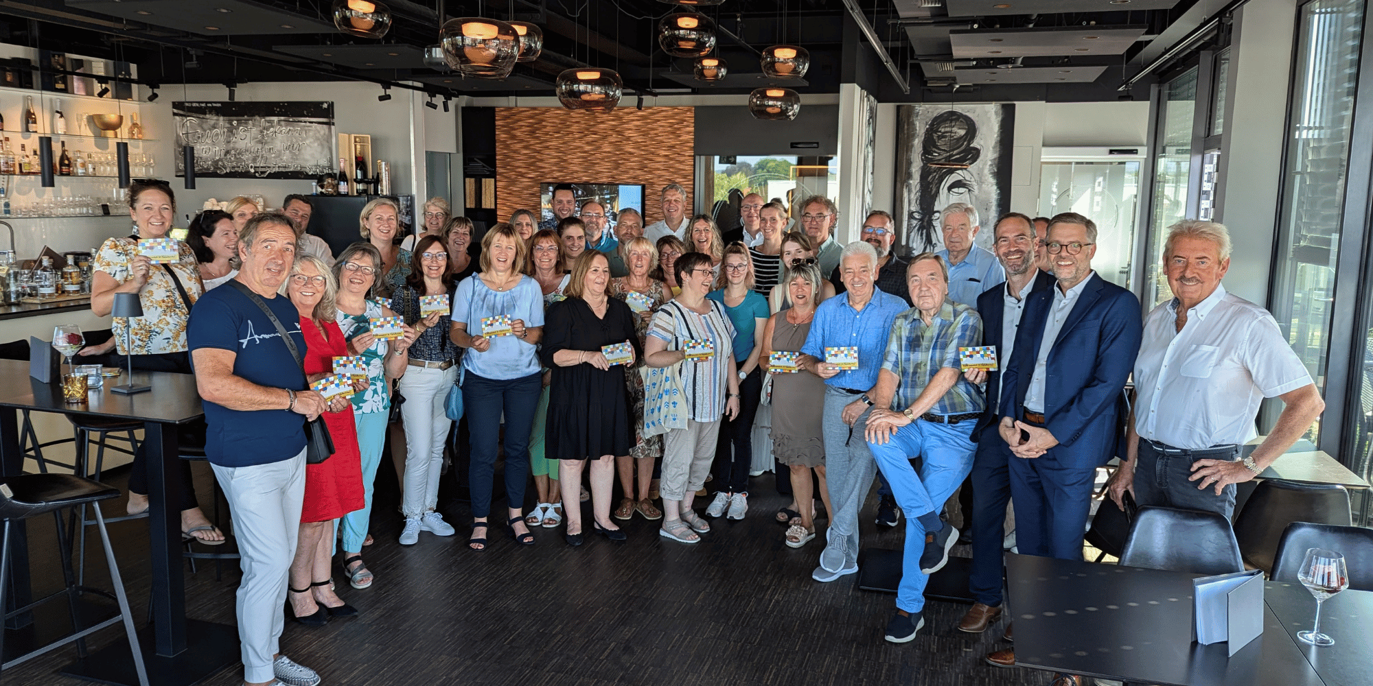 Mehrere Personen stehend und lächelnd mit einem kleinen Heft in der Hand