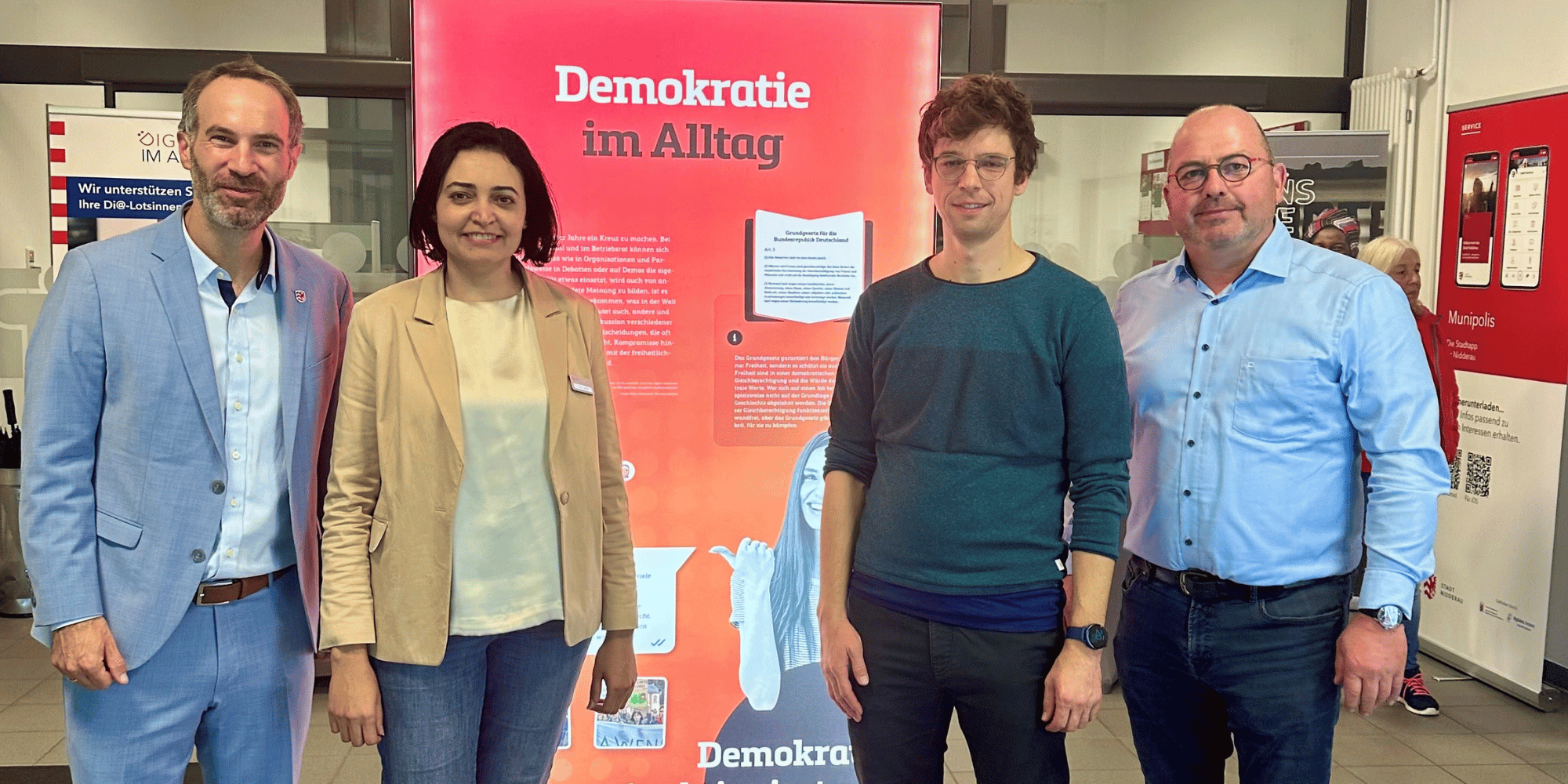 3 Männer und 1 Frau stehend vor einem Banner für eine Ausstellung