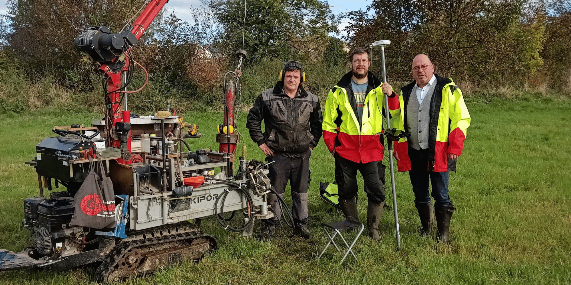 Drei Männer stehend mit einem Arbeitsgerät auf einer Wiese
