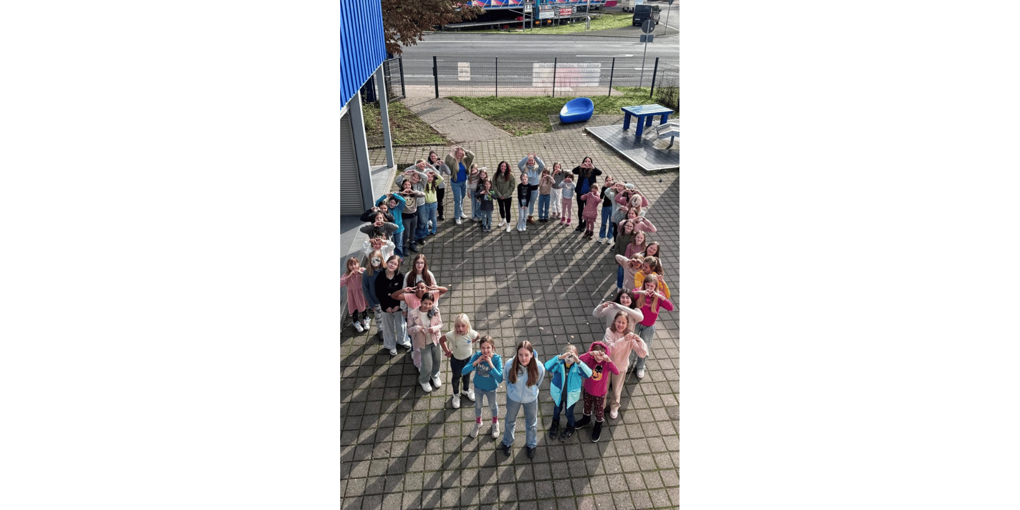 Kinder stellen sich auf einem Hof zu einem großen Herz zusammen