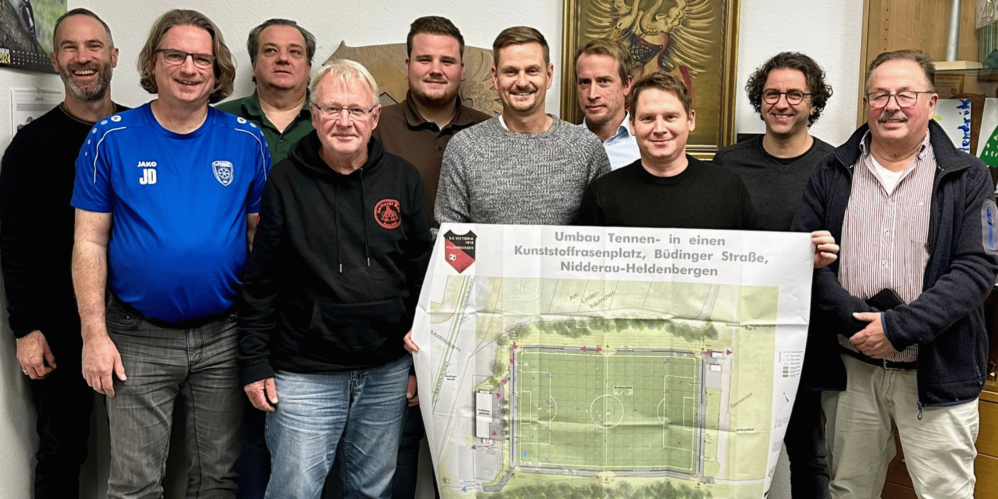 Mehrere Männer stehend mit einem Plakat zu einem Kunstrasenplatz haltend